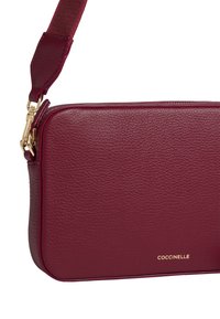 Borsa a tracolla in pelle marrone con superficie texturizzata, hardware dorato e logo del marchio. Presenta una tracolla removibile e una forma rettangolare.