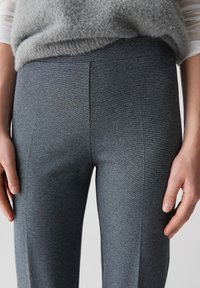 Grijze rekbare broek met een subtiele structuur, voorzien van een slim fit ontwerp en een middelhoge taille, weergegeven met handen op de heupen voor een idee van de pasvorm.