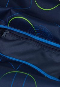 Schwarzer Rucksack-Innenraum mit blauen Reißverschlüssen, ausgestattet mit grünen und blauen kreisförmigen Mustern auf strapazierfähigem Stoff und mehreren Fächern.