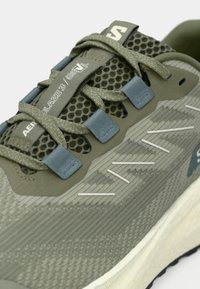 Αθλητικό παπούτσι με επάνω μέρος από ανοιχτό πράσινο δίχτυ που αναπνέει, γαλάζιες λεπτομέρειες και υφασμένο σχέδιο. Διαθέτει λευκό λογότυπο και ευέλικτη σόλα.