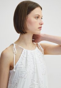 Vestido blanco con bordado floral, con tirantes al cuello y tela suave y fluida. Tiras ajustables en los hombros para un ajuste personalizable.