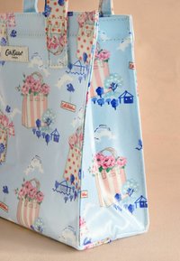 Bolso tote de color azul claro con patrones florales y de casas, que presenta flores rosas, lunares rojos y una etiqueta. Hecho de material duradero.