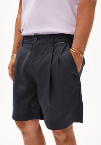 Shorts plissés navy en tissu léger, dotés de poches latérales, d'une fermeture à bouton et d'une étiquette sur la taille avec le logo de la marque.