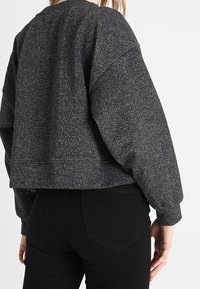 Sudadera negra corta con acabado texturizado, mangas abullonadas y dobladillo acanalado. Lleva puesta con jeans negros de cintura alta.