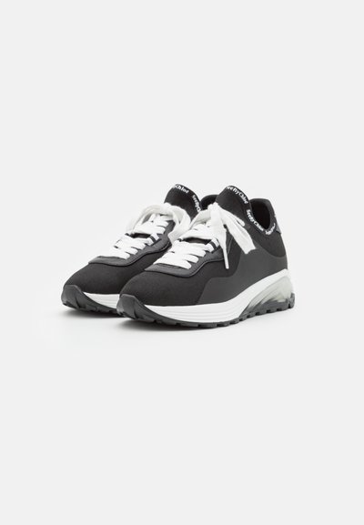 Zwart-witte sport schoenen met een gestructureerde synthetische bovenkant, witte veters en een dikke witte tussenzool. Heeft een doorzichtige buitenzool.