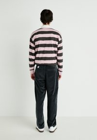 Chemise à manches longues rayée en rose et gris foncé, associée à un pantalon en velours côtelé foncé. Baskets blanches visibles aux pieds. Fond uni.