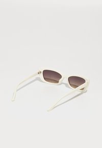 Gafas de sol de plástico blanco con un marco triangular y lentes oscuros de degradado. Las varillas son delgadas con un sutil logo en el lateral.
