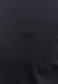 Marineblå strikket polo-shirt med et struktureret mønster, prydet med et lille broderet hestelogo i samme farve på brystet.