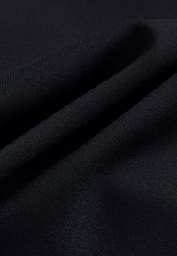 Tessuto nero che mostra una texture liscia e un leggero splendore, con strati piegati che creano linee morbide e fluide. Nessun motivo o accento visibile.