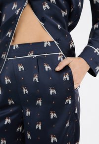 Pijamas de satén azul marino con un patrón de perros, que cuentan con ribetes blancos contrastantes, botones y bolsillos laterales en los pantalones.