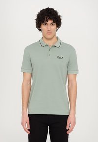 Light green polo shirt with a classic collar, black trim, and EA7 logo on the chest. Short sleeves and a fitted design.