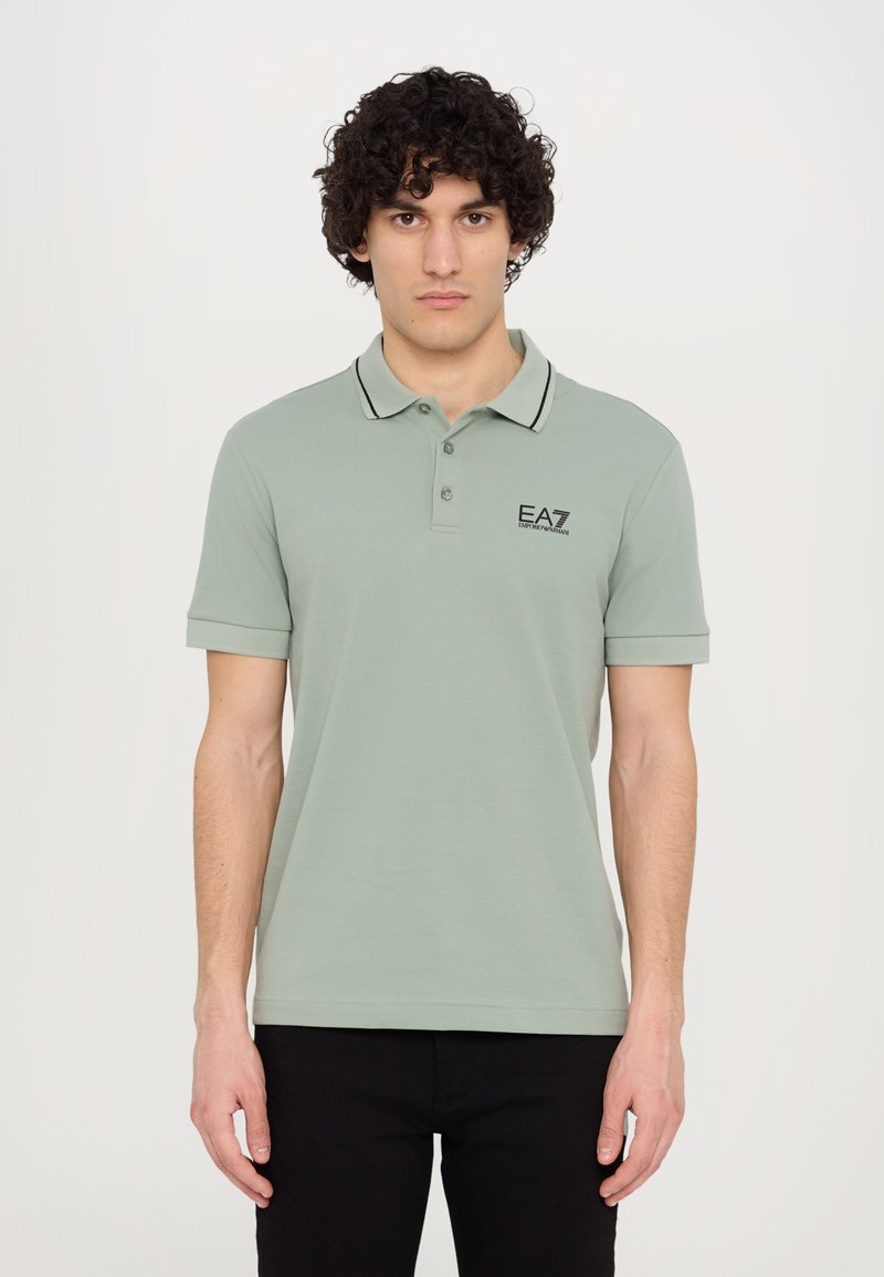 Light green polo shirt with a classic collar, black trim, and EA7 logo on the chest. Short sleeves and a fitted design.