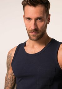 Navyblaues Tanktop aus Baumwolle, mit einem runden Ausschnitt und einer Tasche auf der linken Brustseite. Glatte Textur mit subtilen Nahtdetails.