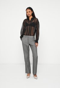 Blusa preta transparente com mangas compridas e fecho de botões frontal, combinada com calças de corte às riscas cinzentas e saltos nude com bico pontiagudo.