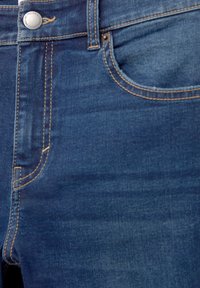Jean en denim bleu foncé avec surpiqûres couleur cuivre, doté d'une poche avant et d'une fermeture par bouton en métal. Tissu lisse avec une légère texture.