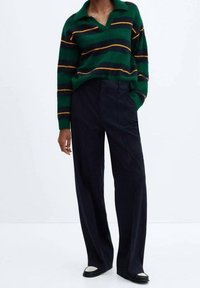 Zielony i granatowy sweter w paski z dekoltem w serek i kołnierzykiem, zestawiony z wysokim stanem, szerokimi spodniami w czarne paski i czarnymi butami.