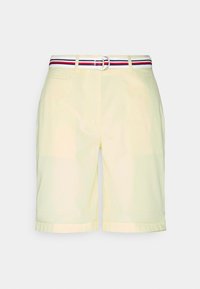 Shorts jaune clair avec une ceinture tressée rouge, blanche et bleue ; comporte deux poches latérales et un ourlet replié en bas.