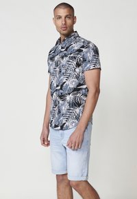 Camicia a maniche corte a stampa floreale bianca e nera in tessuto, abbinata a pantaloni corti di jeans azzurri con risvolti.