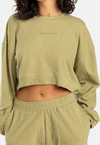 Sweat-shirt vert clair, coupé, avec un col rond et des manches longues. Texture douce avec un logo brodé sur la poitrine. Associé à un pantalon assorti.