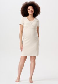 Beige jerseyklänning med korta ärmar och V-ringning. Mjuk textur, figurnära siluett och framträdande korsningsdetalj vid bysten.