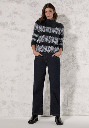 Pull en tricot avec un motif géométrique noir et blanc, col montant et manches longues. Assorti à un pantalon en denim foncé et des bottes noires.