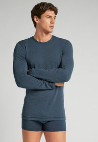 Dunkelblaues langärmeliges Thermaloberteil mit Rundhalsausschnitt, kombiniert mit passenden, enganliegenden Shorts. Beide Teile haben eine glatte, nahtlose Textur.