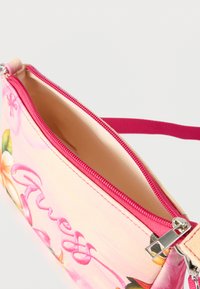 Μικρό ροζ υφασμάτινο πορτοφόλι με λουλουδάτο σχέδιο και κεντημένο το "Guess", με ροζ φερμουάρ και λουρί, εμφανιζόμενο μερικώς ανοιχτό.