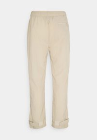 Béžové lehké kalhoty s elastickým pasem, rovnými nohavicemi a nastavitelnými manžetami s uzávěrem na suchý zip. Jedna zadní kapsa.