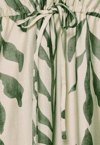 Tissu beige clair avec des motifs de feuilles abstraites vert foncé et un cordon noué à taille froncée.