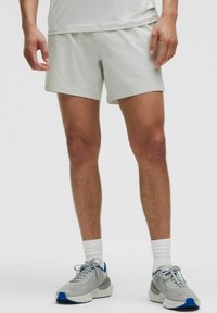 Pantalones cortos atléticos de color gris claro, fabricados con un tejido transpirable, que presentan un ajuste holgado y una textura suave, combinados con zapatillas grises y calcetines blancos de caña corta.
