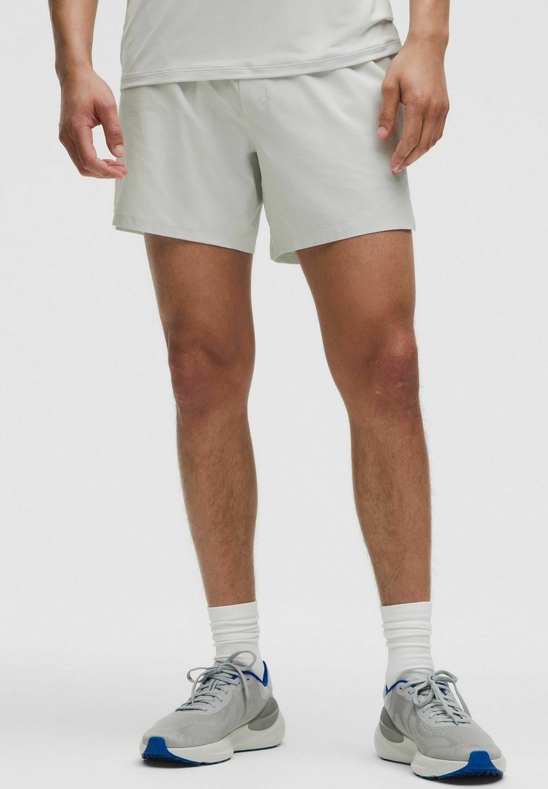 Pantalones cortos atléticos de color gris claro, fabricados con un tejido transpirable, que presentan un ajuste holgado y una textura suave, combinados con zapatillas grises y calcetines blancos de caña corta.