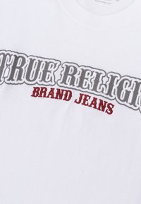 Witte katoenen t-shirt met reliëf grijze en rode borduurseltekst met de woorden "TRUE RELIGION BRAND JEANS" over de borst, ronde hals stijl.
