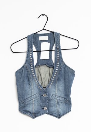 Denimvest met gespsiertrim, twee knopen en voorzakken hangend aan een zwart metalen hanger tegen een witte achtergrond.