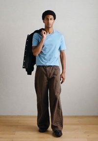 Hele sinine t-särk, pruunid laiad püksid ja must jope üle õla heidetud. Mustad kingad, lihtsa disainiga ja lõdva istuvusega.