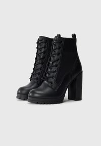 Black ankle boots with a chunky high heel, made of leather and fabric. Features lace-up front and textured sock-like panel for comfort.