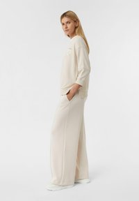 Beige sweatshirt met een ronde hals en driekwartmouwen, gecombineerd met beige broeken met een brede pijp, beide in een zachte stof met minimale detailing.