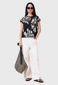 Camiseta de estampado floral negro con mangas cortas, combinada con pantalones anchos blancos. Los accesorios incluyen un bolso texturizado en blanco y negro y sandalias negras.