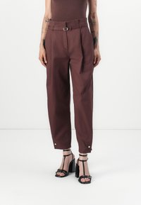 Maroon trousers with belt loops, pleated front, side pockets, and cuffs with snap buttons. Worn with black strappy high-heeled sandals.