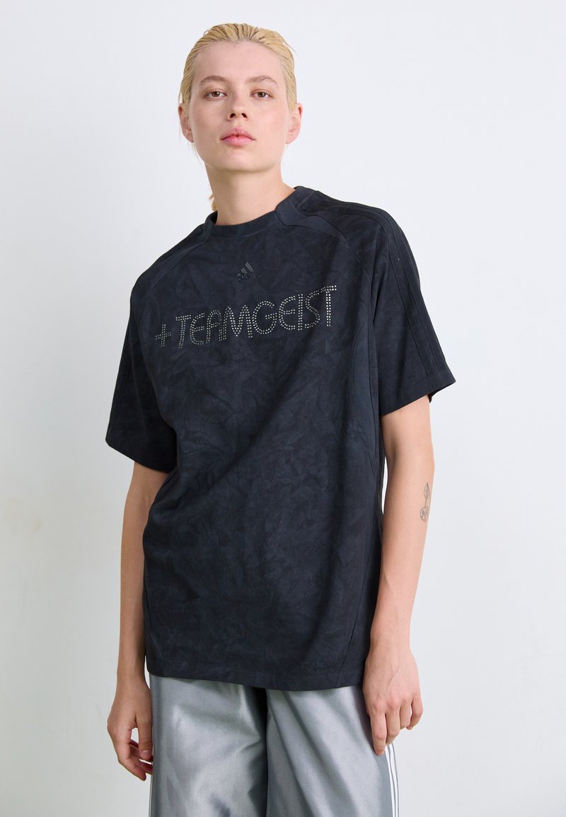 Zwarte t-shirt met korte mouwen met een gestructureerd patroon en "TEAMGEIST" in zilveren studs aan de voorkant. Voorzien van een ronde halslijn en een relaxte pasvorm.