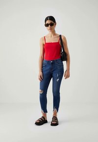 Κόκκινο αμάνικο τοπ, φθαρμένα μπλε τζιν skinny με τριμμένα στρίφωμα και μαύρες χοντρές σανδάλια. Αξεσουάρ περιλαμβάνουν γυαλιά ηλίου και μια μικρή μαύρη τσάντα.