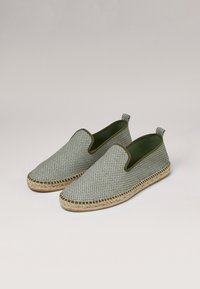 Espadrilles sin cordones hechas de tela con un patrón verde y blanco, con suela de yute trenzado y forro verde oliva, que cuentan con lengüetas en el talón.