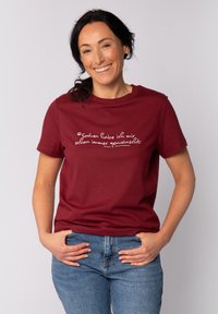 Bordeaux katoenen t-shirt met korte mouwen en een ronde halslijn. Bevat witte tekst in cursief over de borst. Aangesloten ontwerp, gladde textuur.