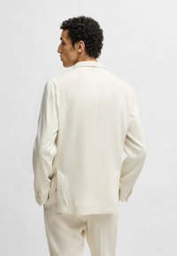 Giacca da abito beige chiaro, vestibilità su misura con una texture liscia, rever a notches e ventaglio sul retro. Decorata con maniche lunghe e dettagli con bottoni.