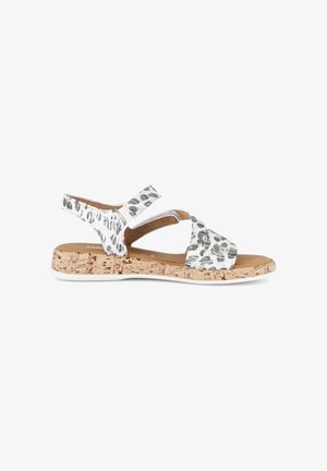 Witte en zwarte sandalen met vlekken, kurken zool, open teen, verstelbare enkelriem en gevoerd voetbed, zijaanzicht.