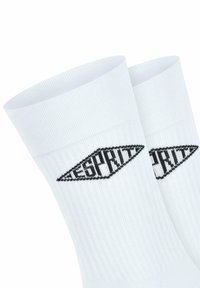 Weiße Baumwoll-Sneakersocken mit geripptem Muster, schwarzem Logo in Diamantform und kontrastierenden Buchstaben an den Seiten.