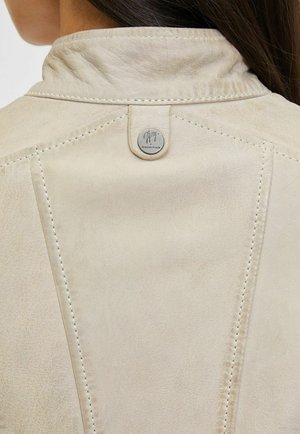 Giacca in pelle beige chiaro con colletto alla mandarino, cuciture a contrasto e una targhetta metallica con logo sulla parte posteriore. Texture liscia con una leggera lucentezza.