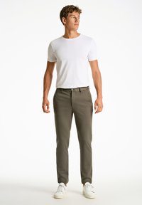 Pantalon ajusté vert olive en tissu doux, doté de passants de ceinture et de poches avant, associé à un t-shirt blanc uni et des baskets blanches.