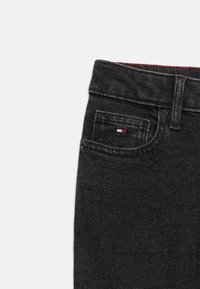 Svarta denimjeans med en frontficka som har en liten röd, vit och blå logotyp samt en texturerad midja. Klassisk femficksdesign.
