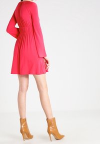 Robe rose à manches courtes avec une taille cintrée et une jupe évasée. Tissu lisse et encolure ronde, assortie à des bottines à talons hauts couleur tan.
