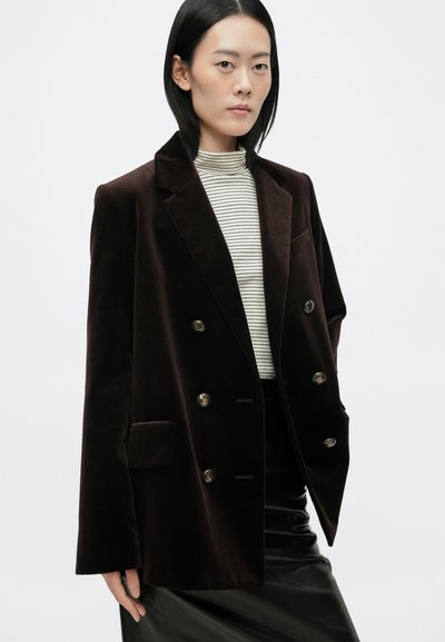 Brun fløjl dobbeltradet blazer med klassiske revers, to forlommer og dekorative metalknapper, parret med en stribet top.